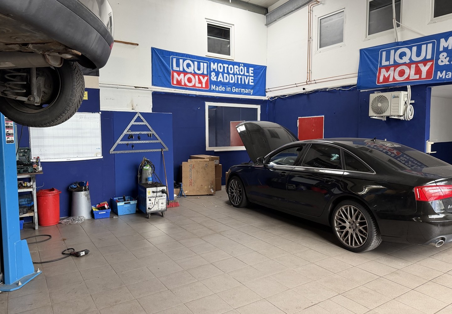 Blick in die Werkstatt: ein Fahrzeug mit geöffneter Motorhaube neben der Hebebühne.